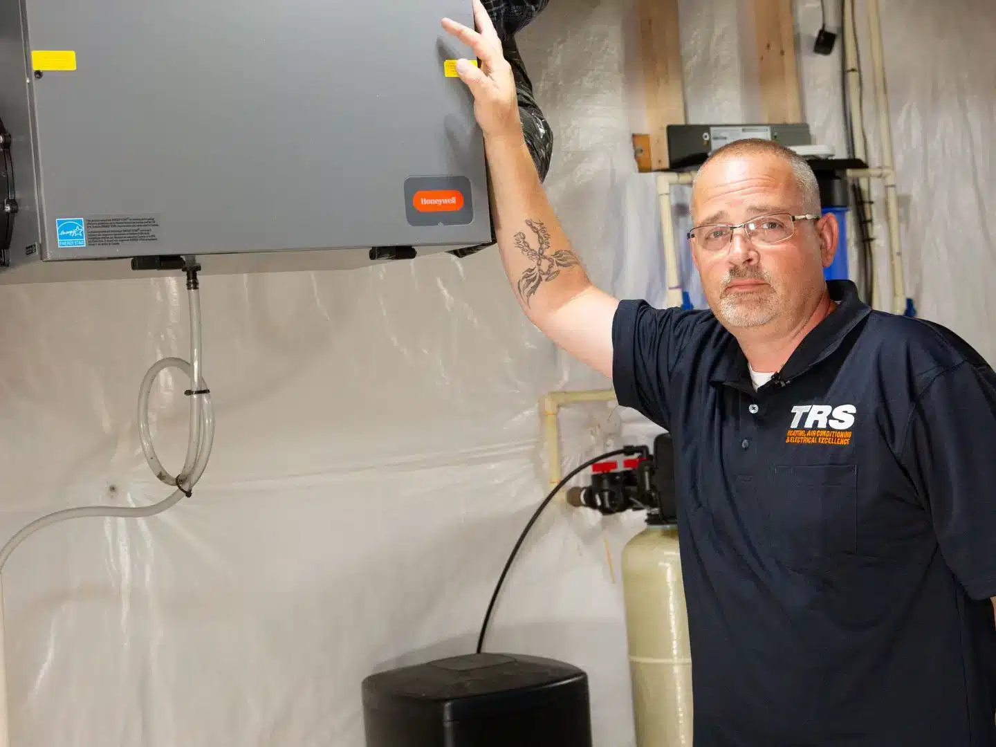 An HVAC technician next to a dehumidifier in a basement.